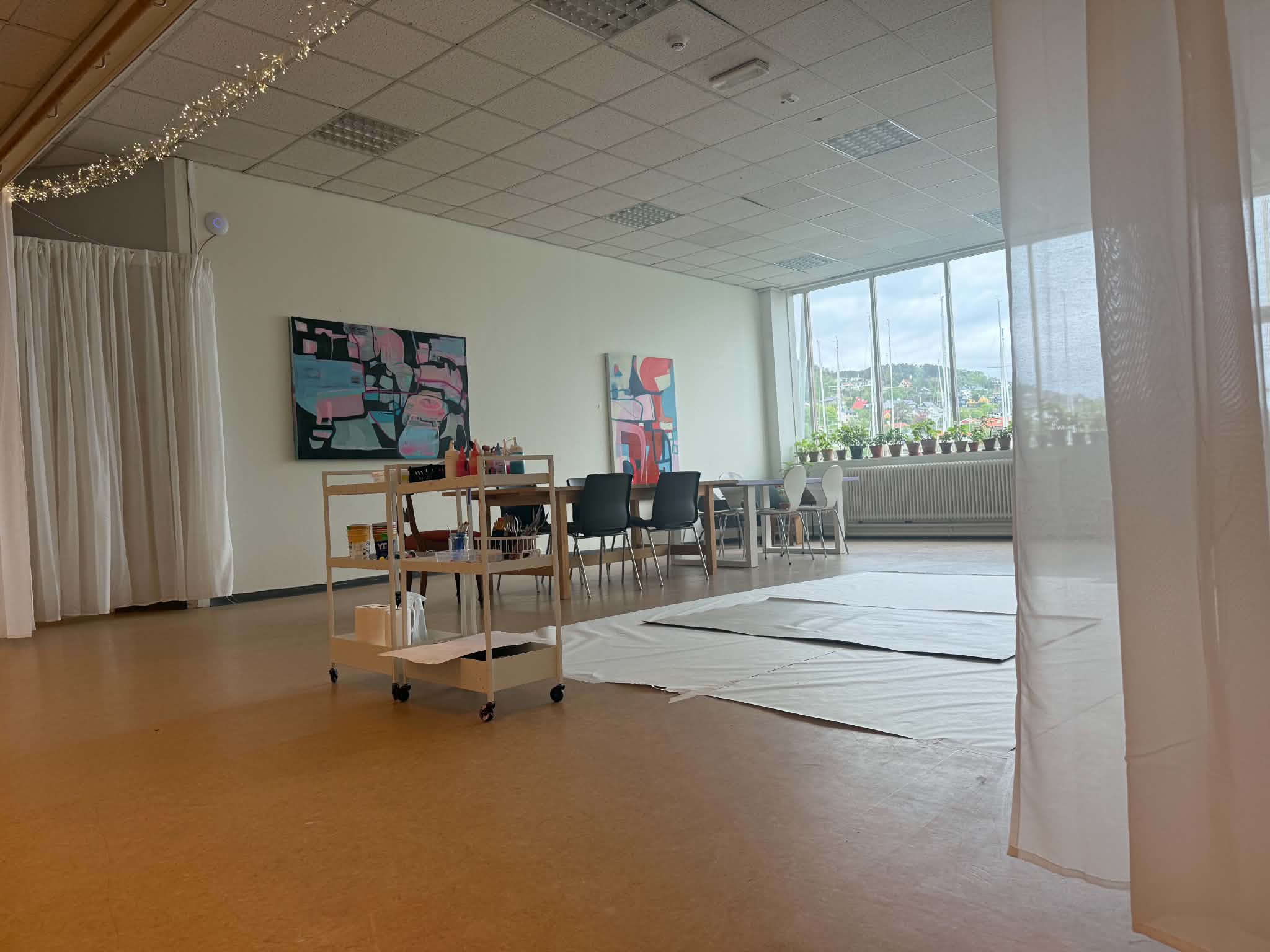 Atelieret med lerret på gulvet, malerier på veggen og lyslenker